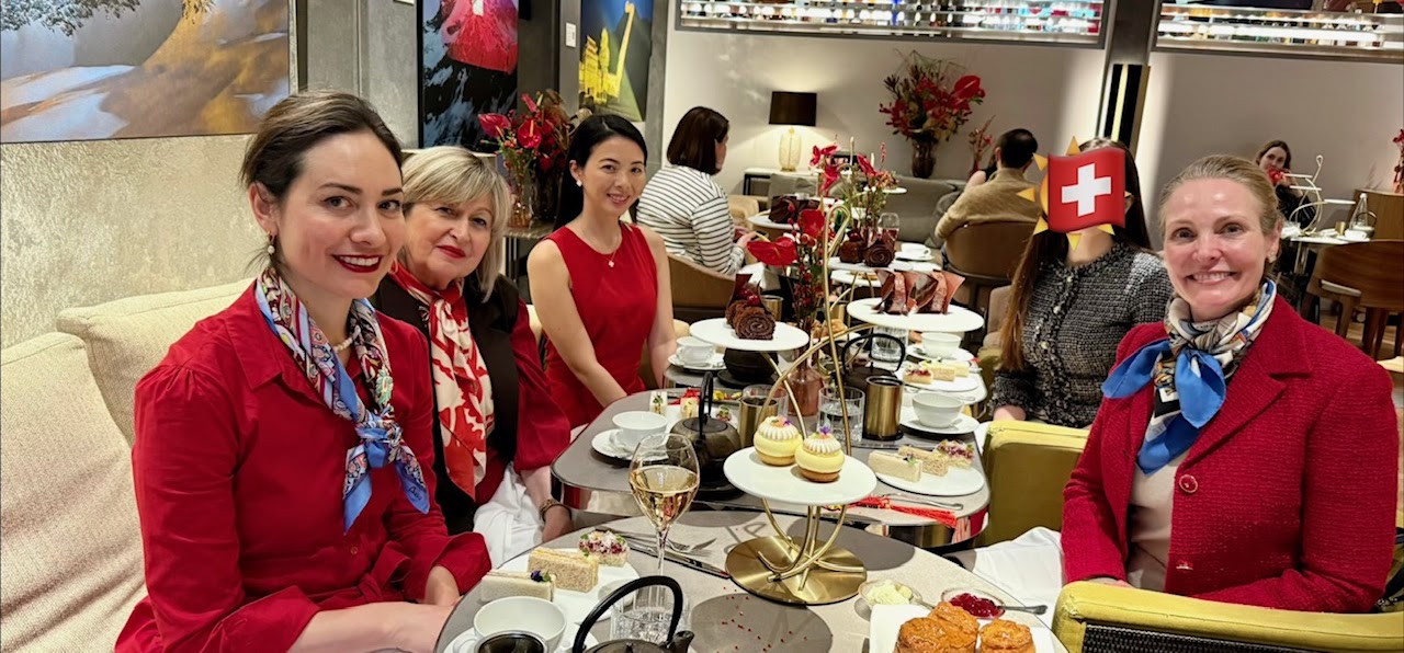 Four club members dressed in red at a festive afternoon tea, with tiered stands of pastries, scones and champagne
