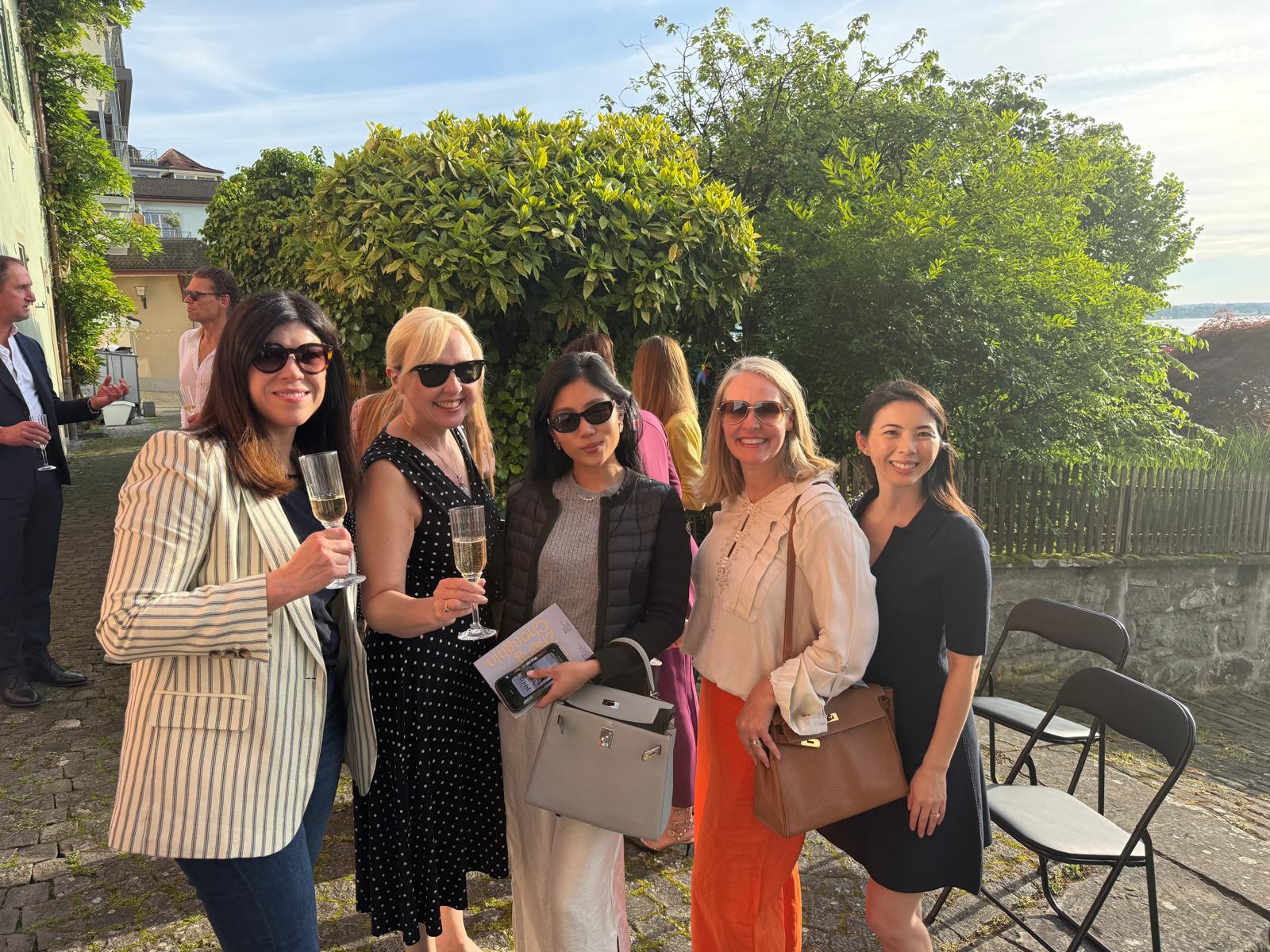 Members with glasses of champagne in a cobbled courtyard garden on a summer evening