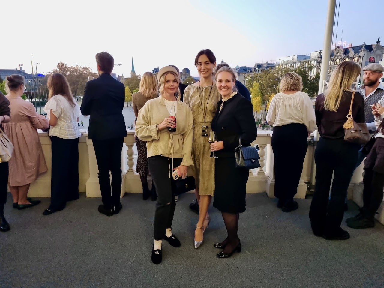 Three members at an evening reception on a terrace overlooking the river and Zurich old town